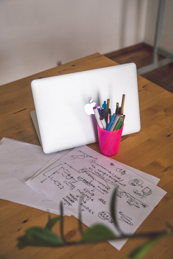 A desk featuring a laptop, notes, and colorful pens in an indoor office setting.